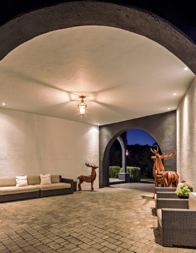 Elegant outdoor lounge area with archway, modern seating, and decorative deer sculptures at dusk.